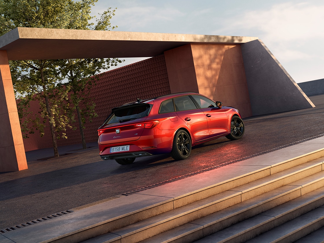 Glossy black mirror covers for the seat leon Sportstourer fr contrasting with the red car body, side view with cement background.