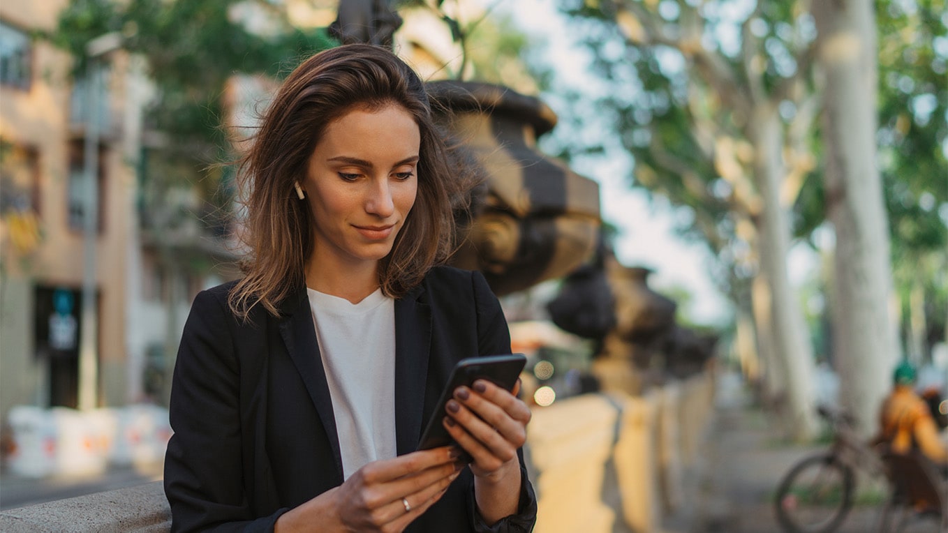 Woman using mobile phone to for seat connect, standing against concrete wall in the middle of the city.