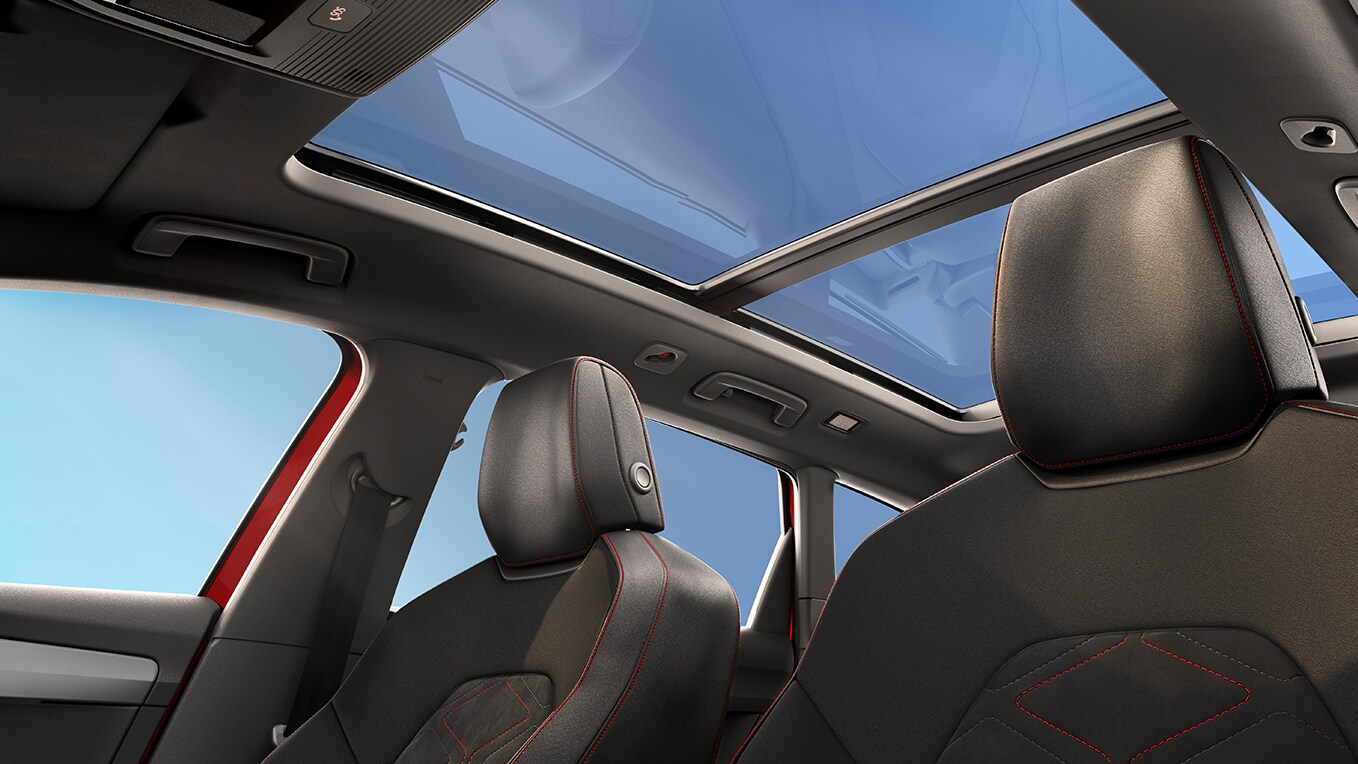 Interior view of seat car with panoramic sunroof and passenger in vibrant red outfit, showing the spacious cabin design.