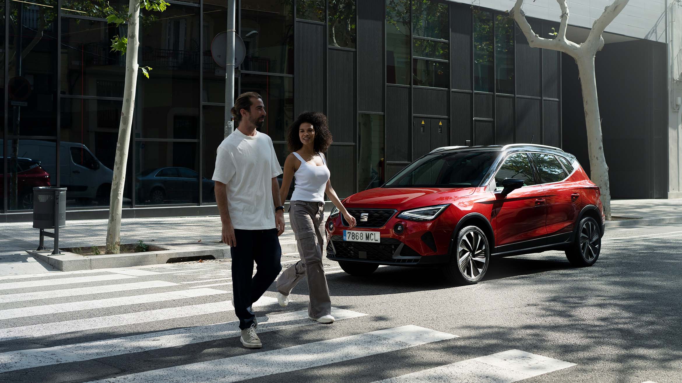 man and woman crossing the street together near SEAT Arona in desire red color parked behind them.
