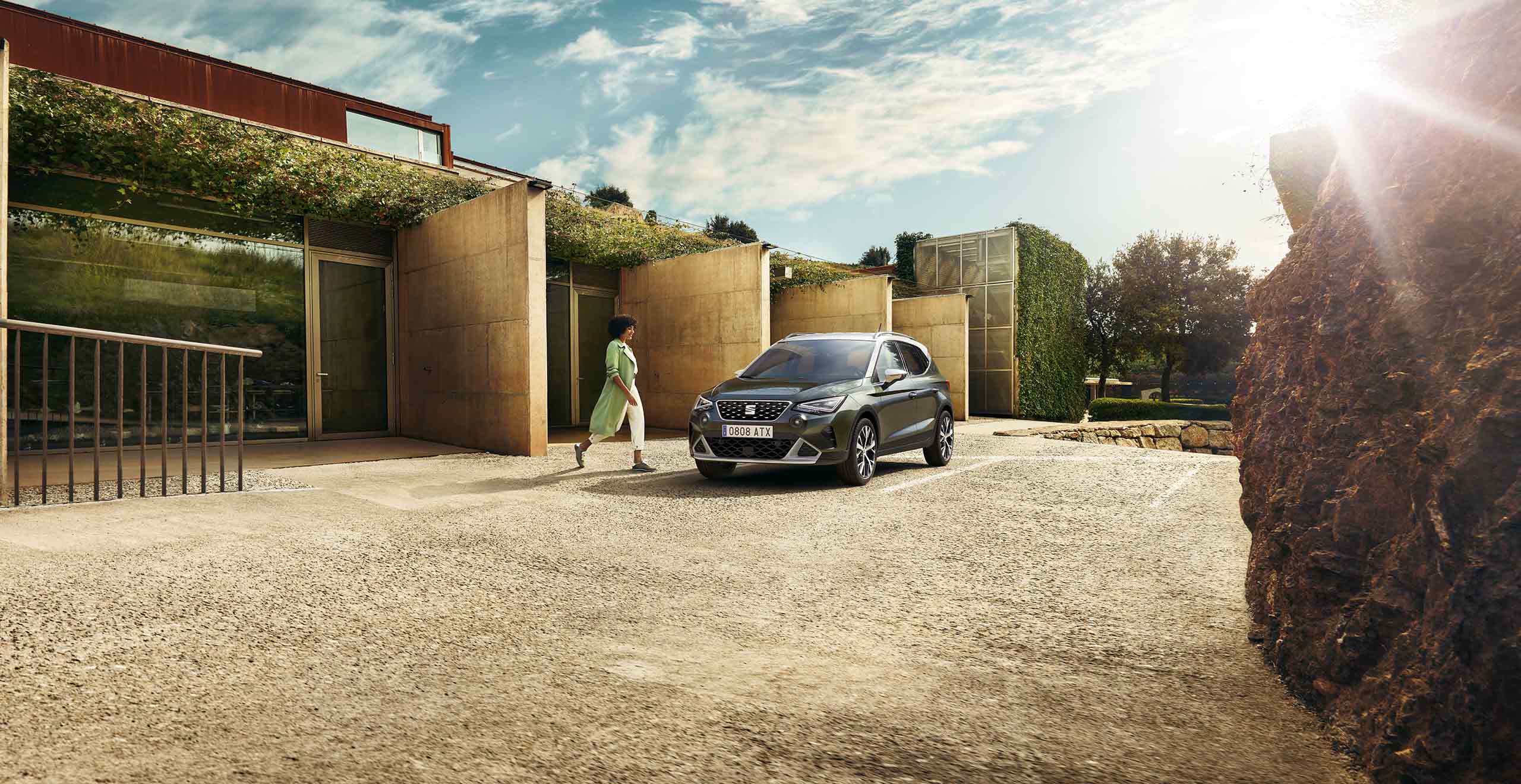 Woman walking to SEAT Arona dark camouflage colour with a candy white roof. 