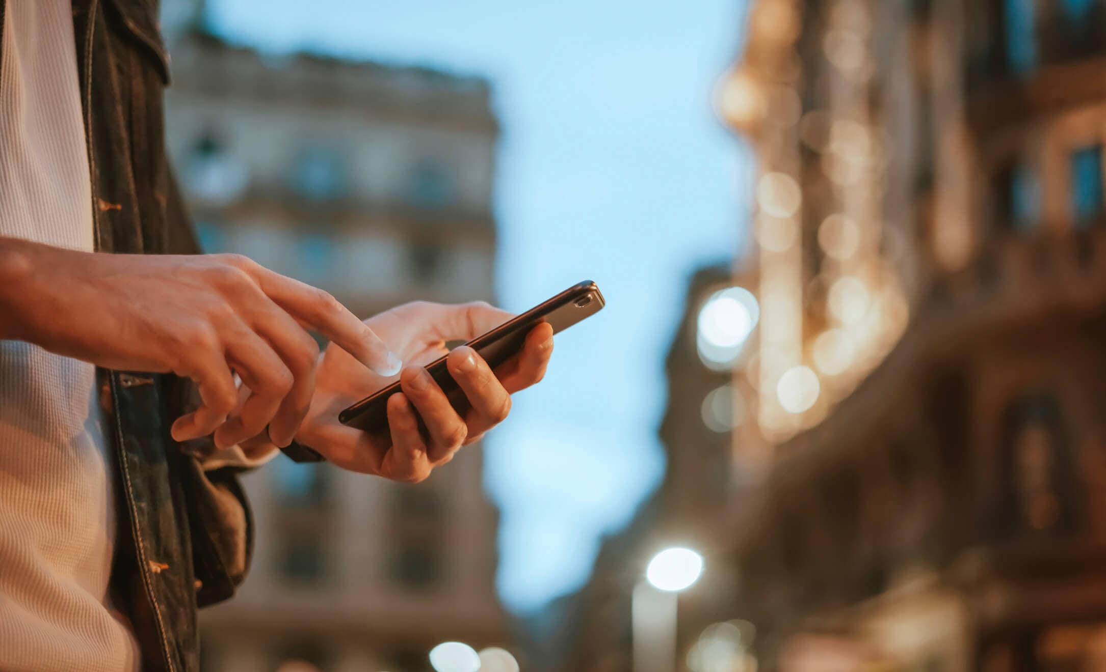 partial view of a man interacting with his phone and the background of the city with buildings and lights