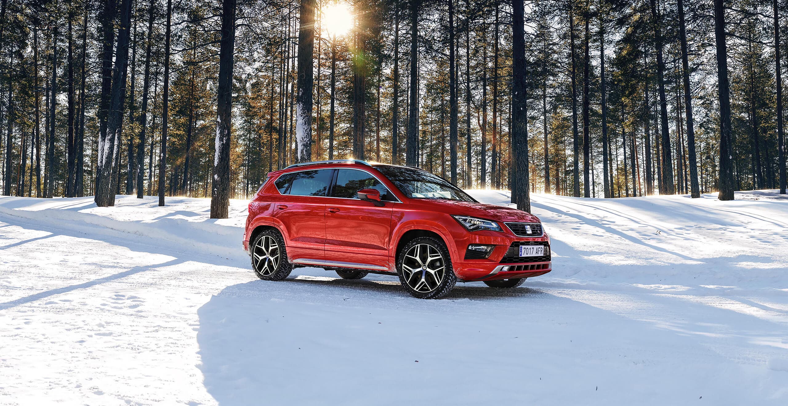 Red SEAT Ateca SUV car driving in snowy woods in front of tall trees